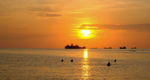 Silhouette people swimming in sea against sky during sunset