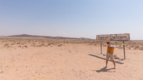 Full length of woman standing by signboard against clear sky