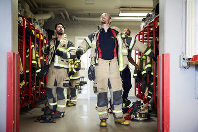 Firefighters looking up while wearing protective workwear in locker room at fire station