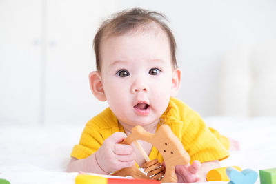 Healthy asian baby girl in yellow bodysuit playing with wooden toys on white bedding