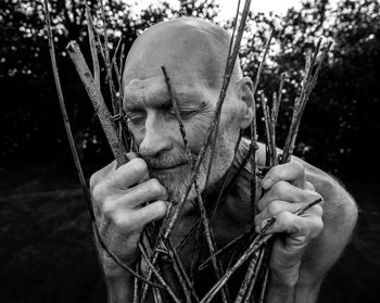 Close-up of shirtless man holding branches outdoors