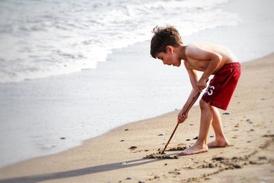 Side view of shirtless boy playing with sand at beach