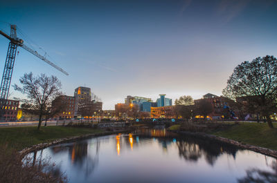 River by illuminated buildings against sky at dusk