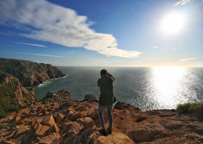 Woman standing on rock by sea against sky