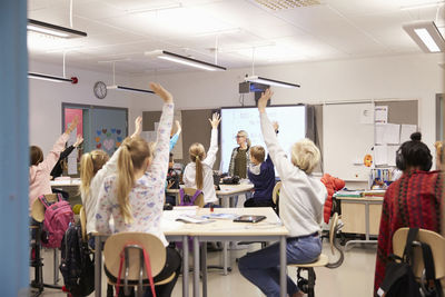 Teacher looking at students with arms raised in classroom