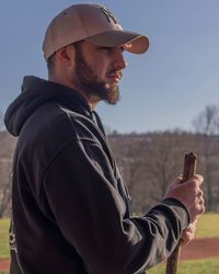 Side view of young man holding stick while standing against clear sky during sunny day