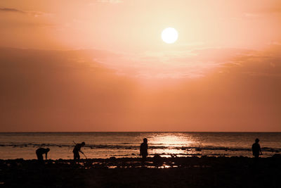 Silhouette people on beach against sky during sunset