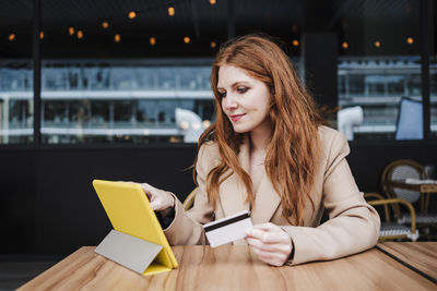 Young woman using phone while sitting on table