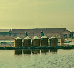 People on lake by house against clear sky