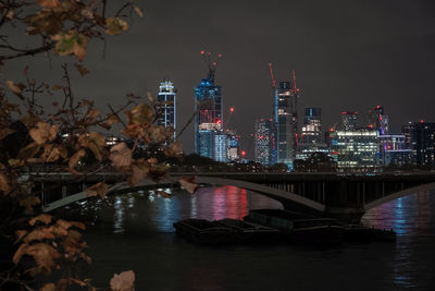 Illuminated bridge over river by buildings against sky at night
