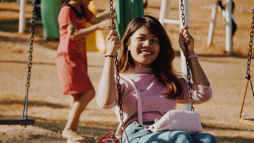 Happy young woman looking away while swinging at park