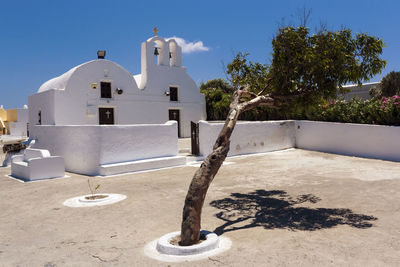 Cross by tree outside building against sky