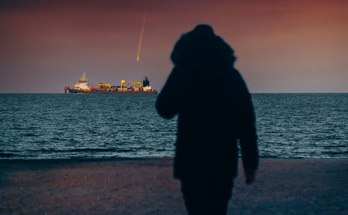 Silhouette man standing on beach against ship and sky during sunset