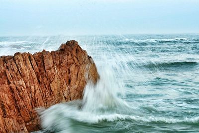 Wave splashing on rock formation in sea against sky