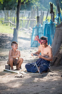 Shirtless boy sitting by craftsperson on ground