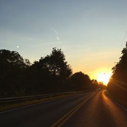 Road by trees against sky during sunset