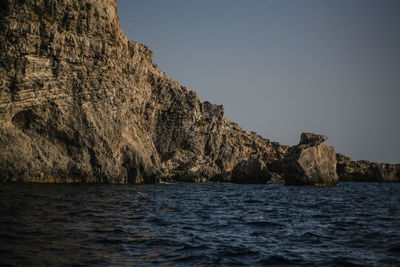 Rock formation by sea against clear sky