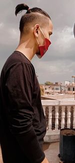 Side view of young man standing against sky with face mask