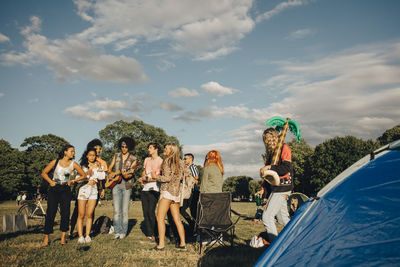 Multi-ethnic friends enjoying music in event against sky on sunny day