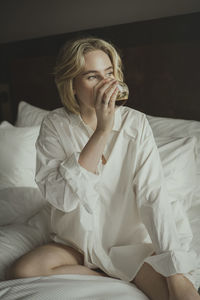 Blond woman drinking in bedroom