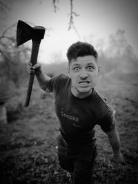 Portrait of angry man with axe standing on field