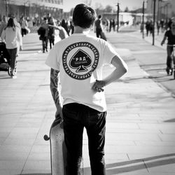 Rear view of man with skateboard standing on footpath