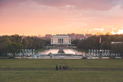 Visitors watching lincoln memorial against pink sunset sky.