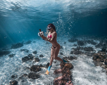 Full length of woman holding camera in sea