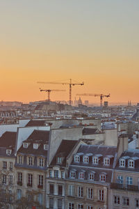 Construction site by buildings against sky during sunset