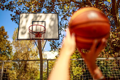 Cropped hands holding basketball against hoop