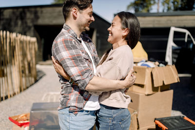 Happy couple embracing while standing outside new house during sunny day