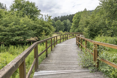 Bridge made of wooden boards over a green field with trees and wooded hills