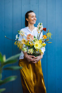 Young woman in flowing yellow skirt and white shirt with beautiful bouquet of peonies in glass vase