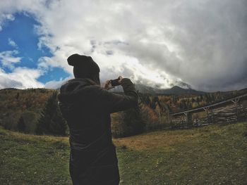 Rear view of man standing on grassy field against sky