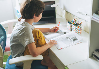 Rear view of boy sitting on table at home