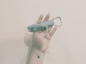 Close-up of cropped hand holding penknife with bottle opener against beige background