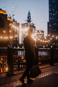 Rear view of woman standing on illuminated railing at night