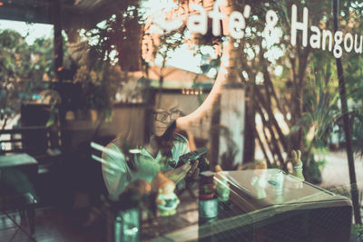 Woman using phone in cafe seen through window