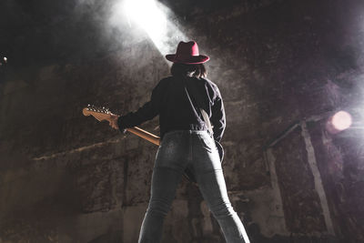 Rear view of woman playing guitar by wall at concert