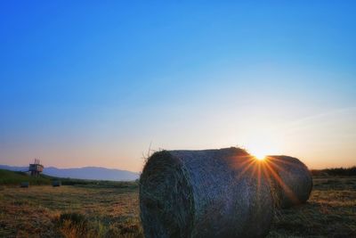 Hay bales on field against clear sky at sunset