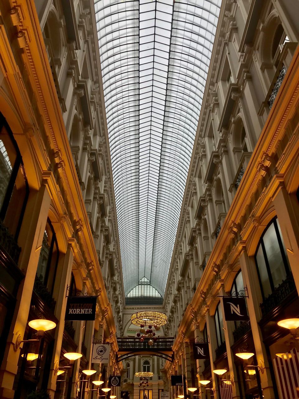 architecture, built structure, ceiling, low angle view, shopping mall, indoors, illuminated, travel, lighting equipment, building, modern, city, travel destinations, incidental people, day, tourism, diminishing perspective, arcade, architectural column, electric lamp