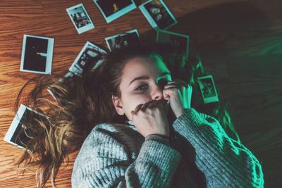 High angle view of woman lying with scattered instant transfer print on hardwood floor