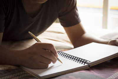 Midsection of woman writing in book on bed