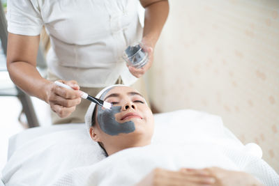 Midsection of beautician applying face mask to customer