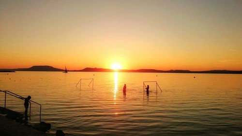 Silhouette man in sea against clear sky during sunset