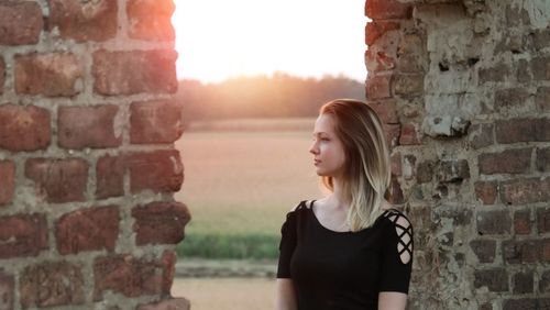 Thoughtful young woman looking away while standing by brick wall