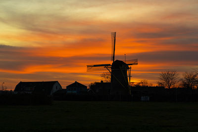 Silhouette buildings on field against orange sky