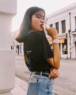 Young woman looking away while standing on street in city