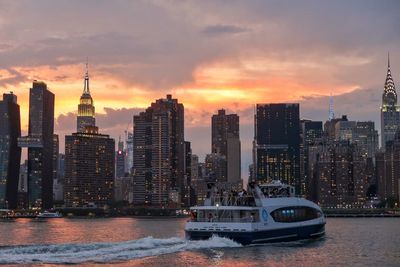 Boat sailing in river against modern buildings during sunset