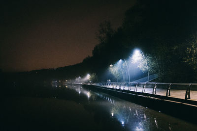 Illuminated bridge over river against sky at night